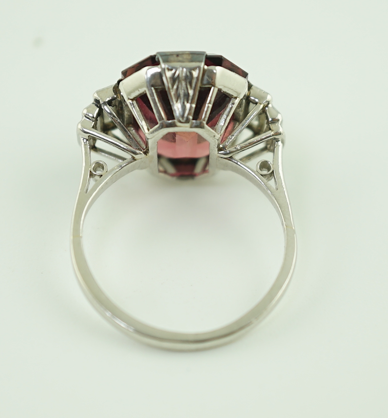 An Art Deco platinum and single stone emerald cut deep pink tourmaline set dress ring, with graduated six stone baguette cut diamond set shoulders